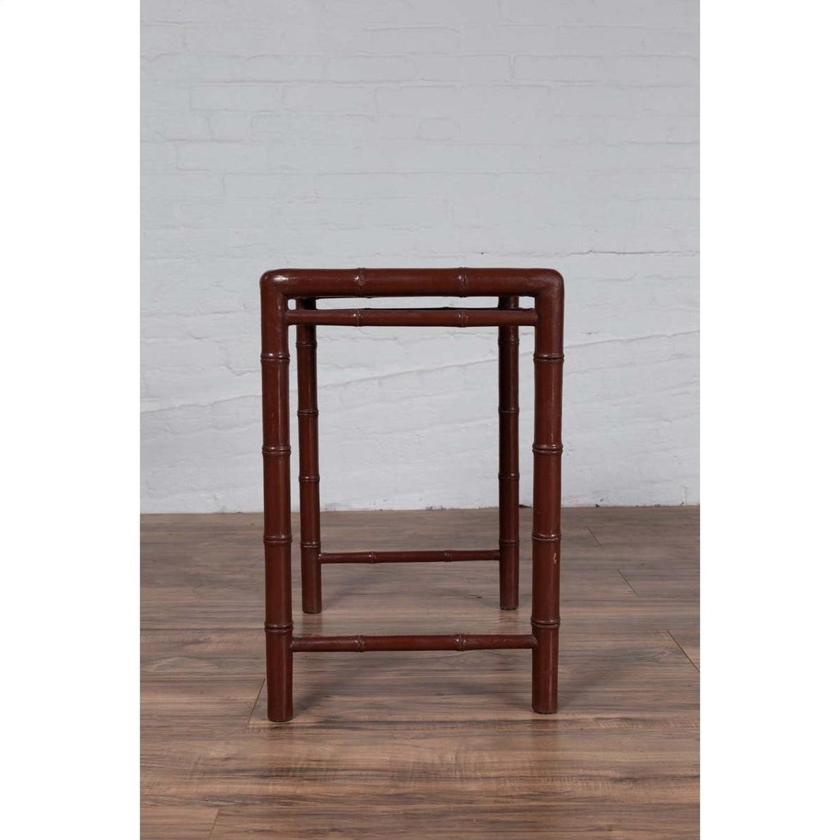 Brown bamboo side table with vintage patina on wooden floor, white brick wall background, 1950s Chinese design.
