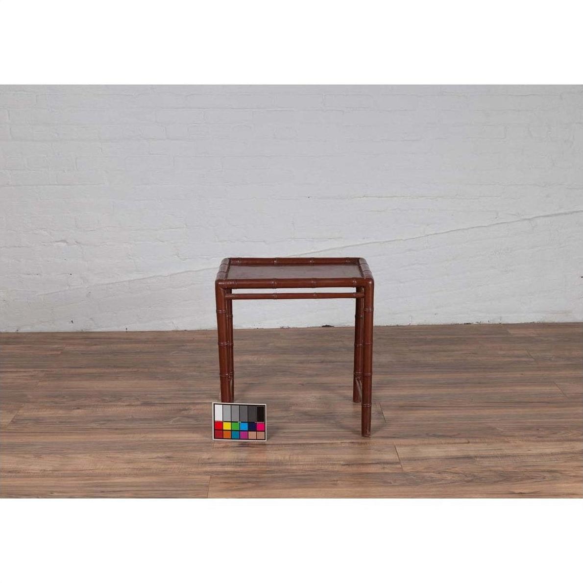 Brown bamboo side table with vintage patina, placed on wooden floor against white brick wall and color chart.