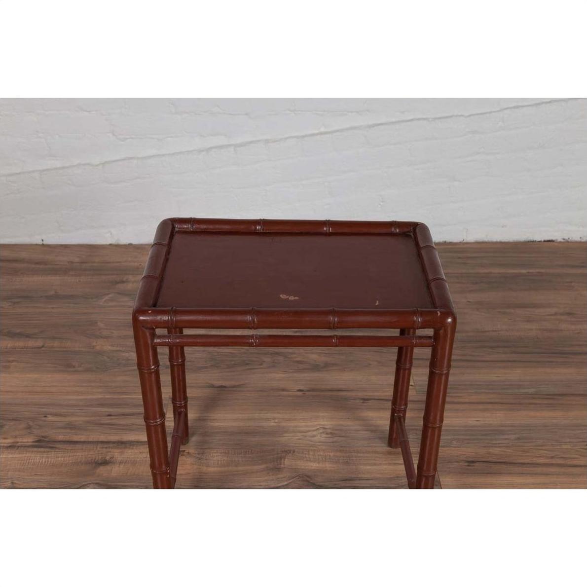 Brown bamboo side table with vintage patina on wood floor, white brick wall background, indoor setting.