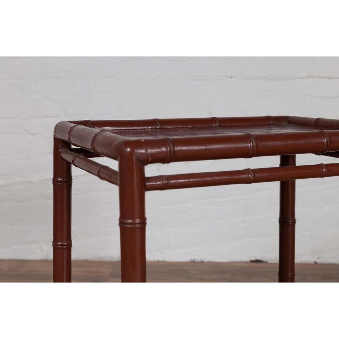 Brown bamboo side table with recessed top, vintage 1950s, against white brick wall and wood floor indoors.