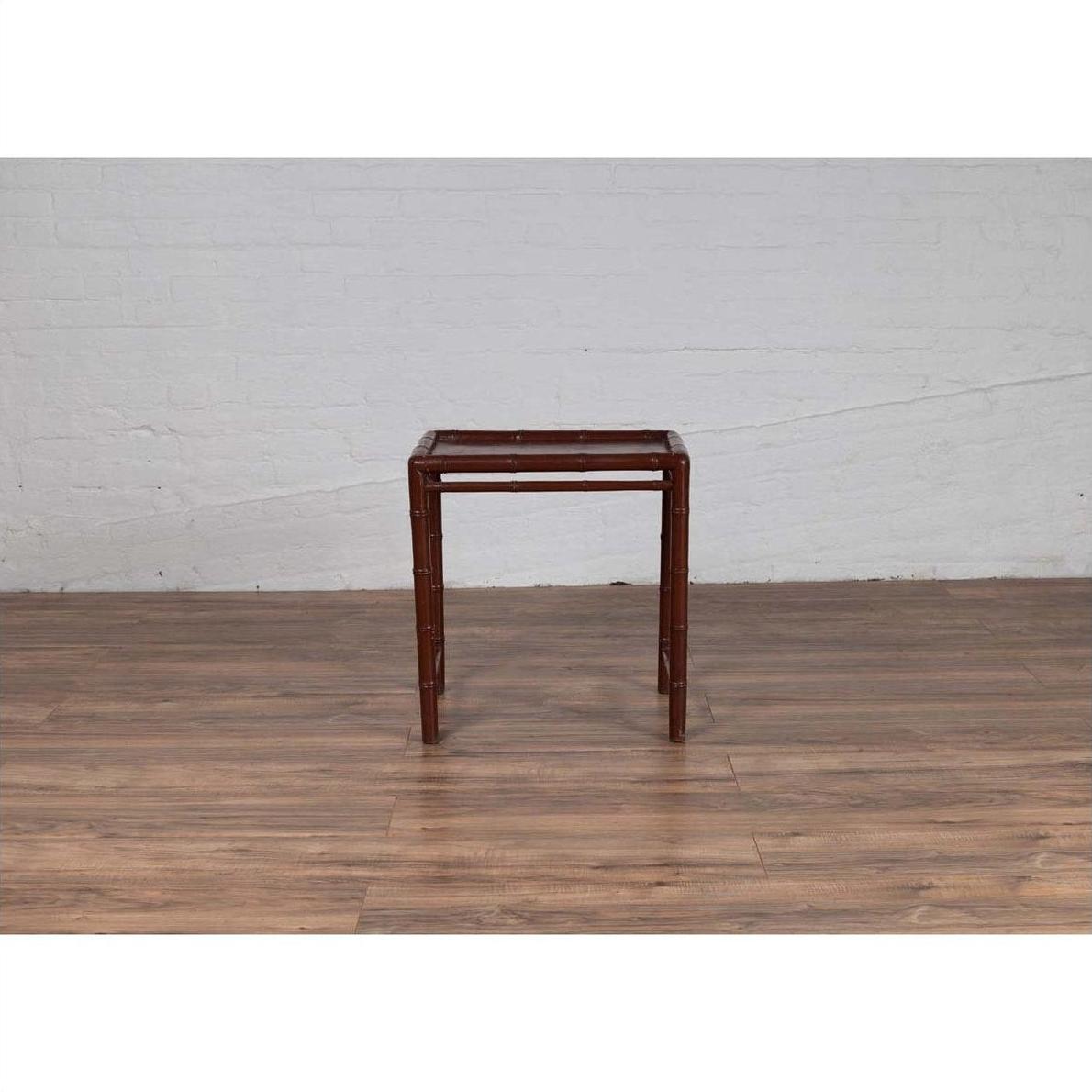 Brown bamboo side table with recessed top on wooden floor next to white brick wall, vintage 1950s Chinese style.