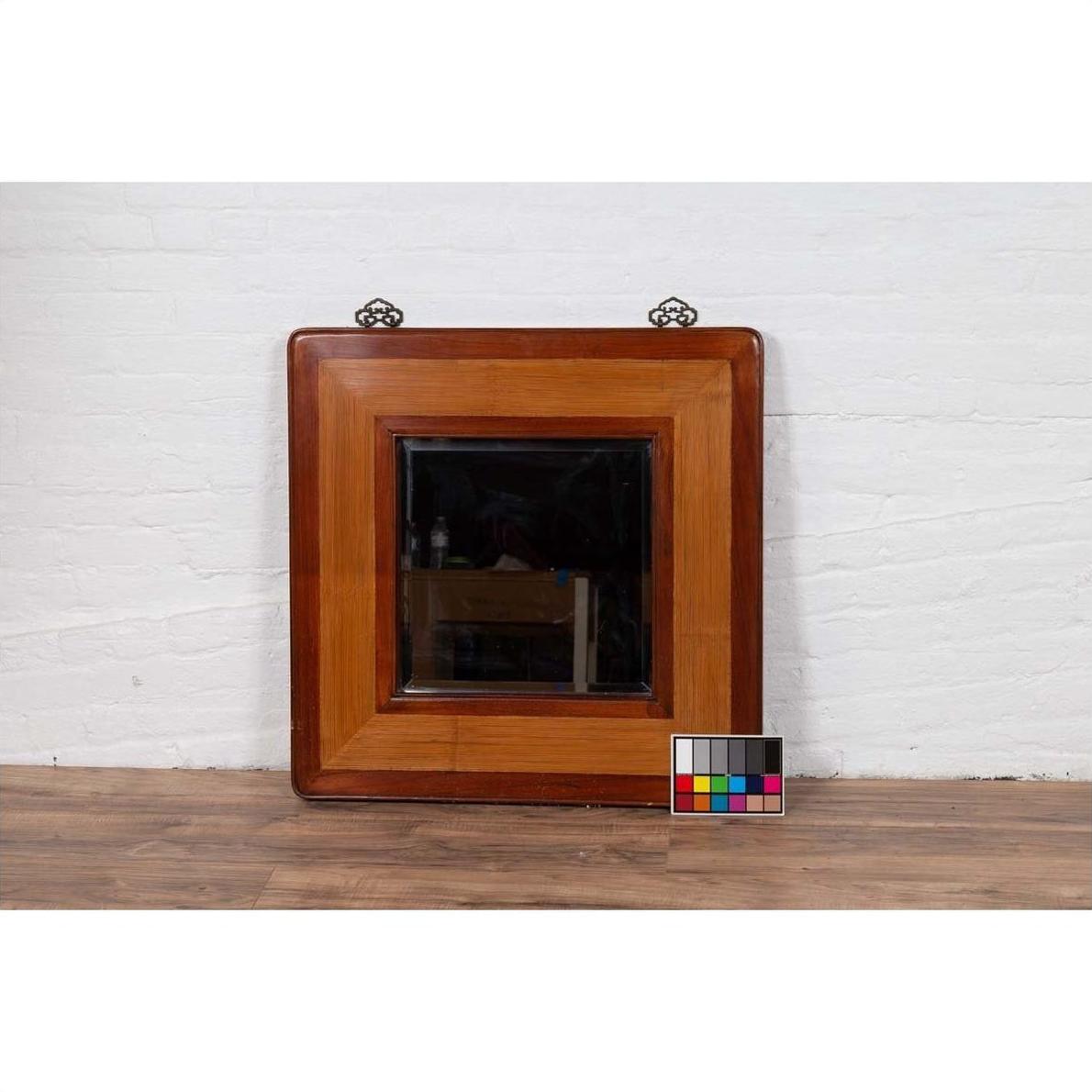 Two-toned elm and rattan square mirror with beveled glass, vintage 1950s Chinese style, against white brick wall.