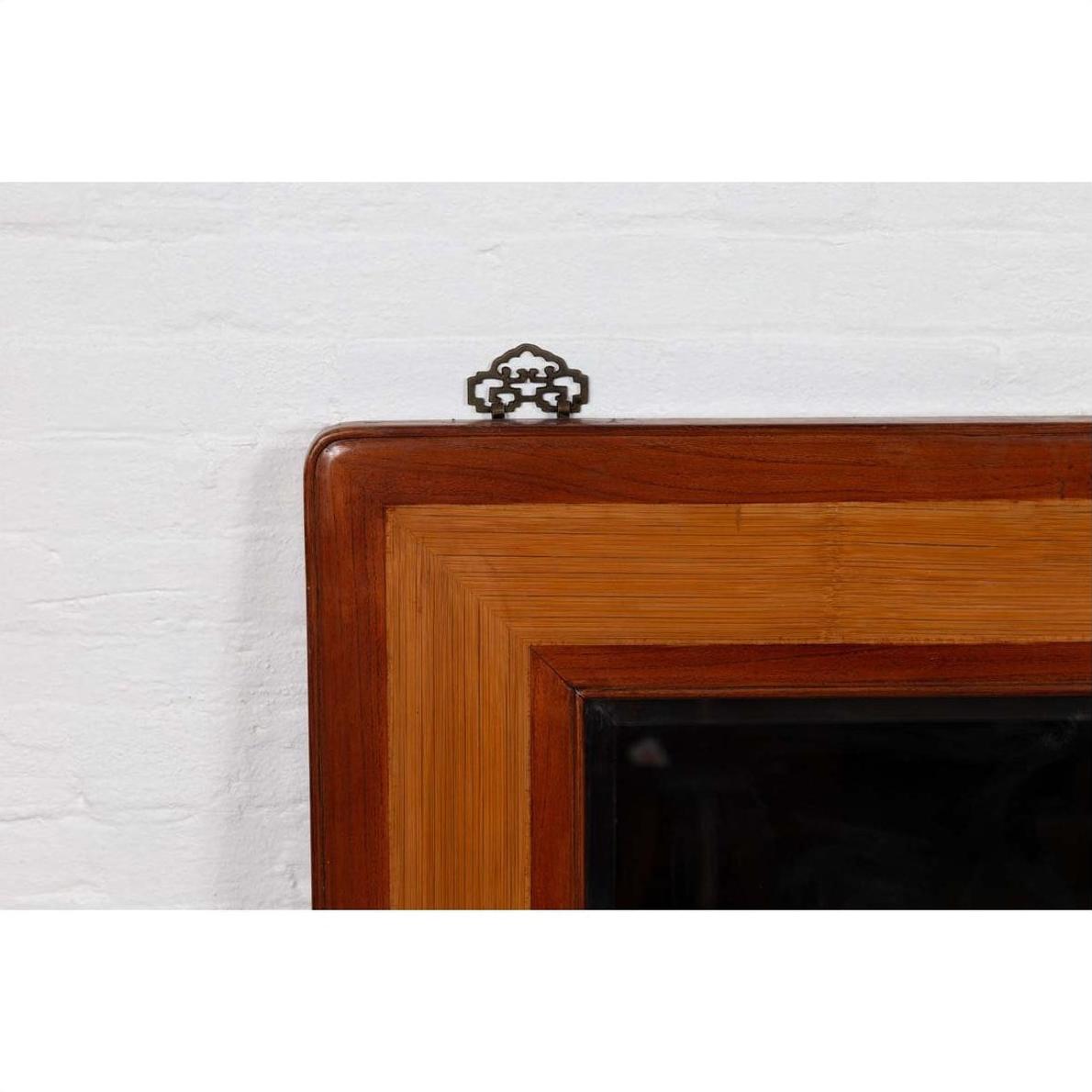 Close-up of vintage Chinese 1950s elm and rattan mirror with beveled glass and metal hanger against white wall.