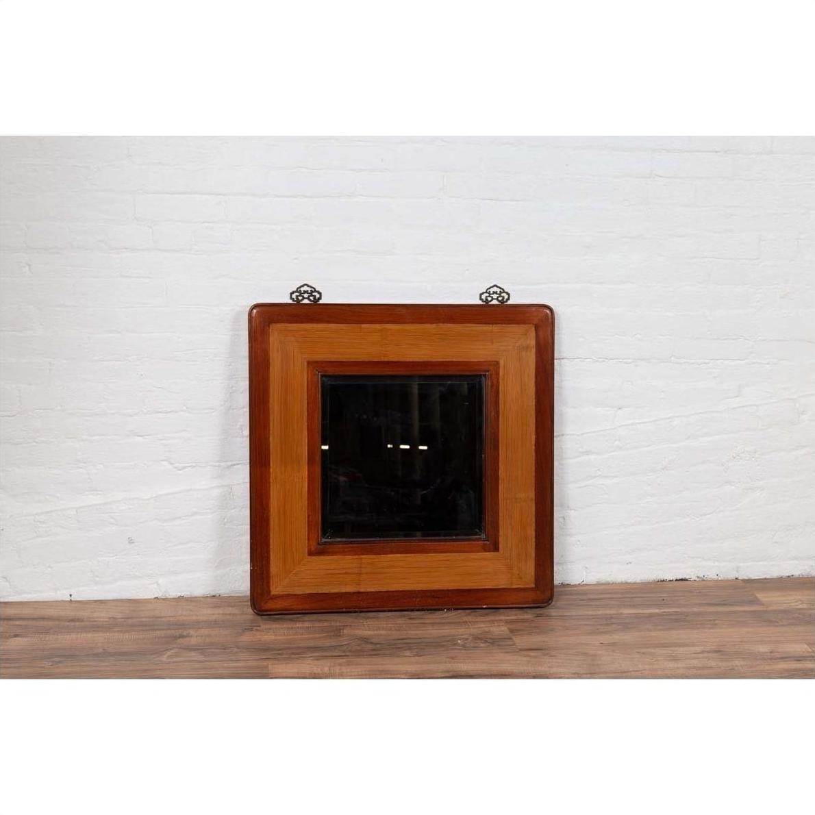 Two-toned elm and rattan square mirror with beveled glass, vintage 1950s Chinese style, against white brick wall.