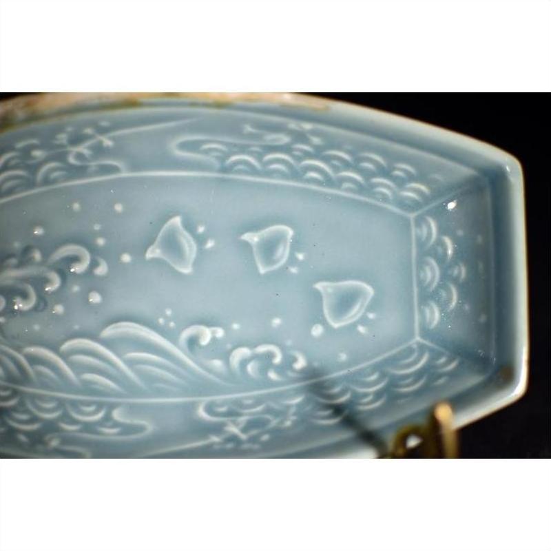 Close-up of green celadon ceramic dish with embossed fish and wave patterns.