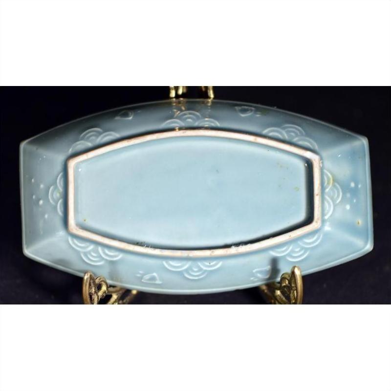Green celadon ceramic dish with floral patterns on a metal stand, set against a dark background.