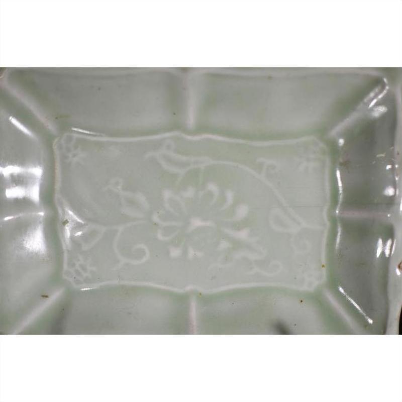 Pale green celadon ceramic dish with subtle floral and scroll designs, close-up of center pattern.