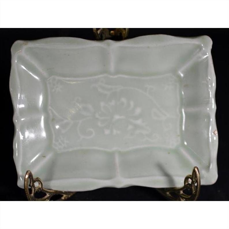 Green celadon ceramic dish with raised floral motif on metal stand, close-up home decor piece.