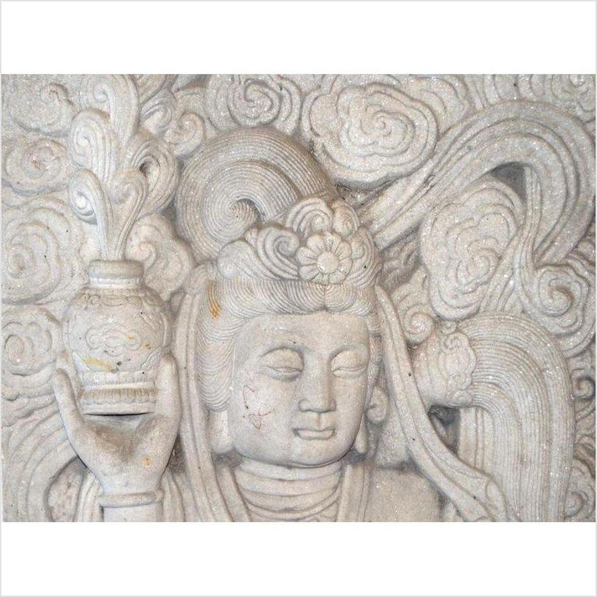 White stone Bodhisattva sculpture with closed eyes, hand-carved, holding a vase among swirling clouds.