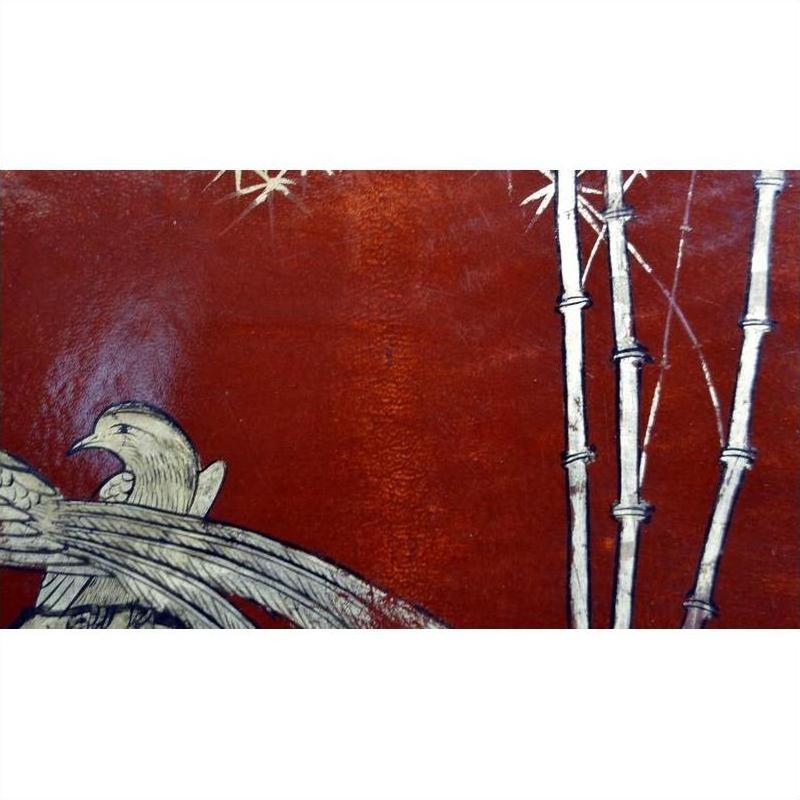 Close-up of red lacquered Chinese dowry box with hand-painted bird and bamboo design on textured background.