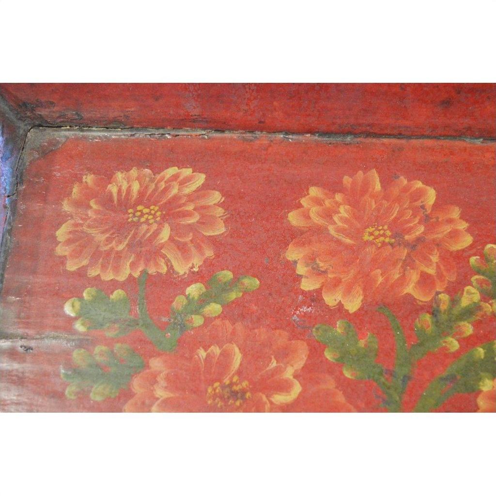 Red metal tray with hand-painted orange flowers and green leaves, ornate design, close-up.