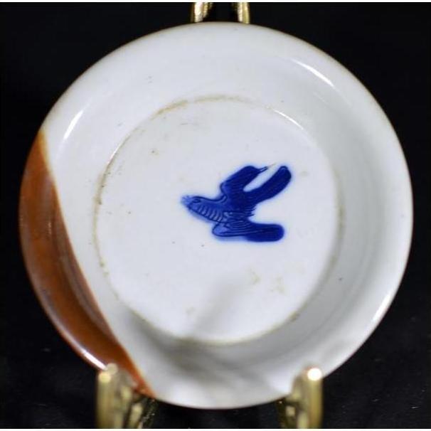 Close-up of vintage Chinese porcelain dish with brown rim and blue bird mark visible on the underside.