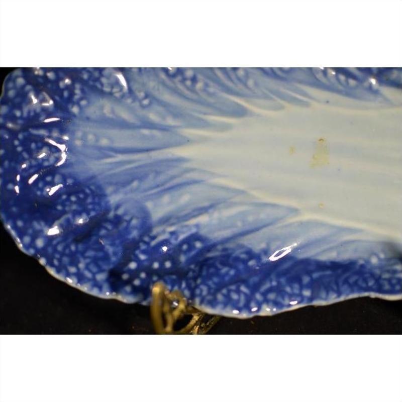 Close-up of blue and white porcelain dish with hand-painted design and textured, leaf-like edge.