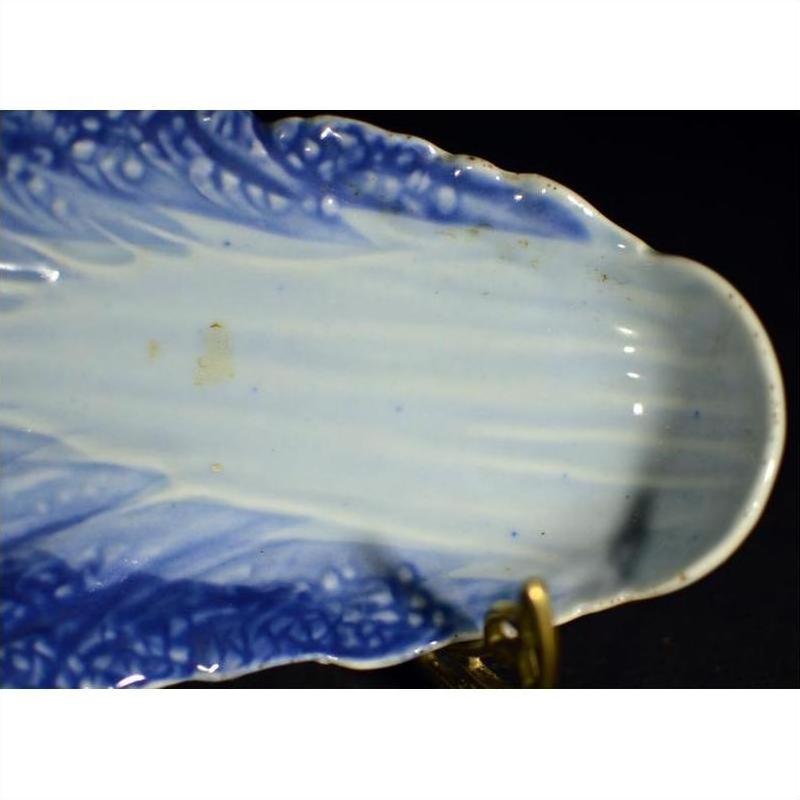 Close-up of blue and white porcelain dish with hand-painted leaf pattern and scalloped edge, displayed on a stand.