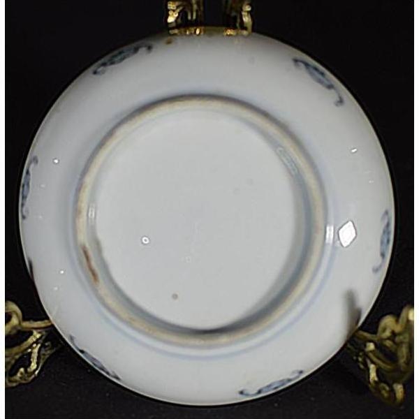 Close-up of the underside of a white porcelain vintage Chinese plate on a brass stand with dark background.