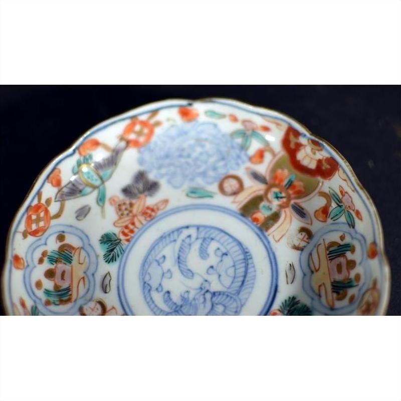 Close-up of vintage Chinese porcelain plate with blue, orange, and green hand painted patterns on dark background.