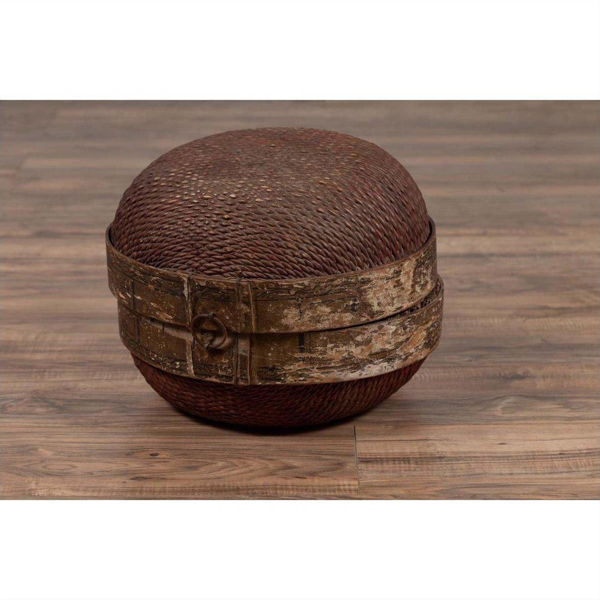 Brown rattan circular hat box with weathered patina on a wooden floor indoors.
