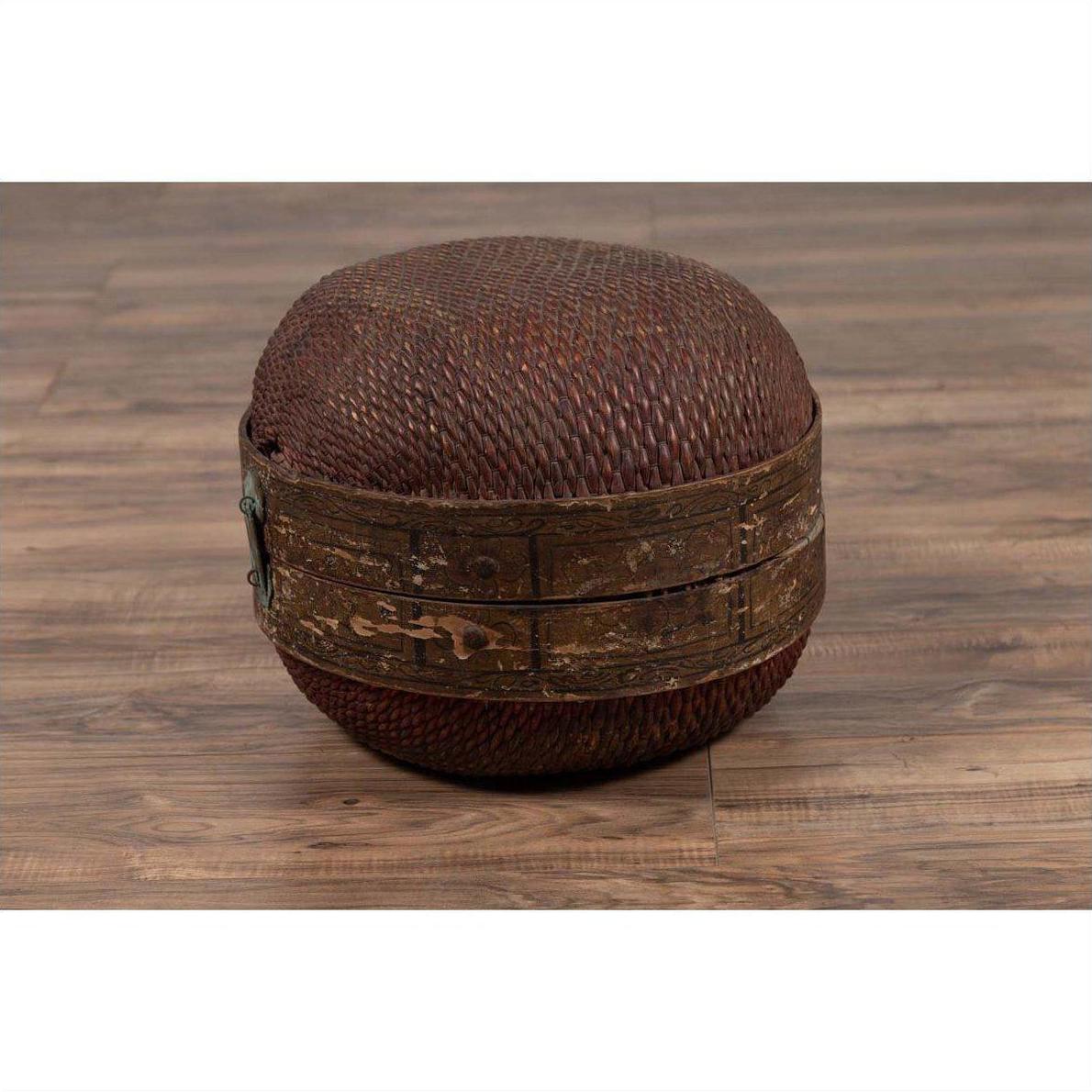 Brown rattan hat box with weathered patina on a wooden floor.