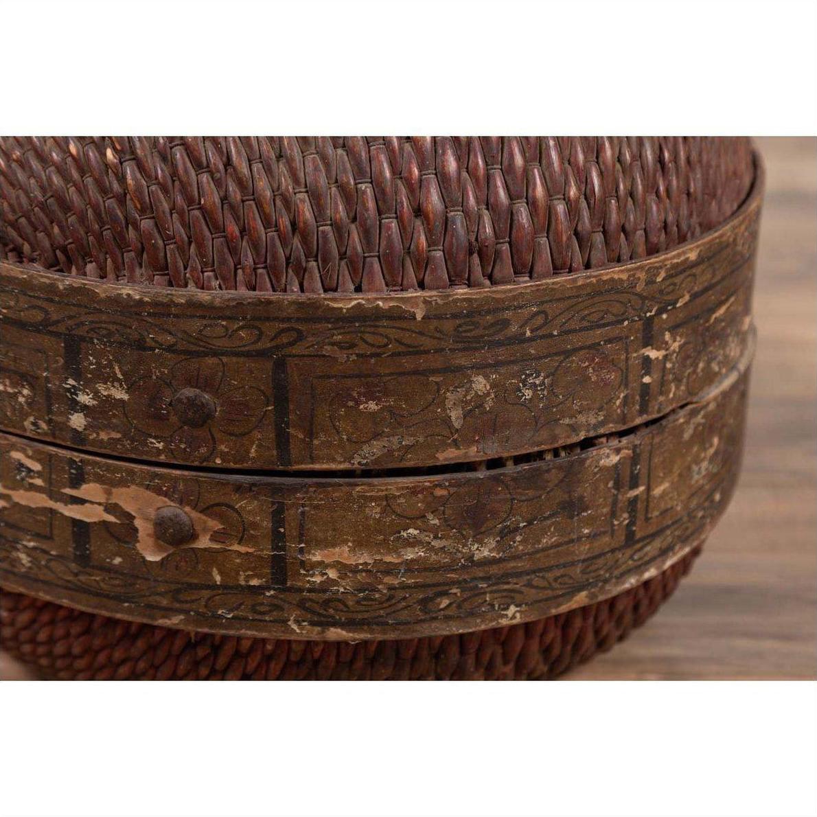 Close-up of a brown rattan circular hat box with weathered patina and faded floral patterns.