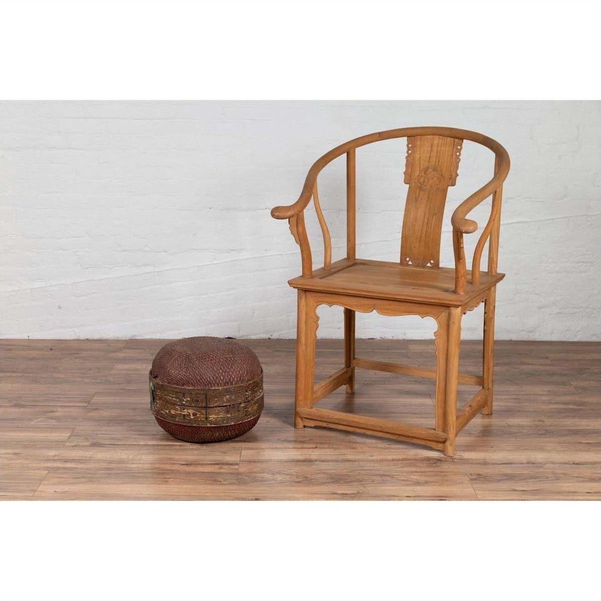 Brown rattan circular hat box with weathered patina beside a wooden armchair on a wood floor indoors.