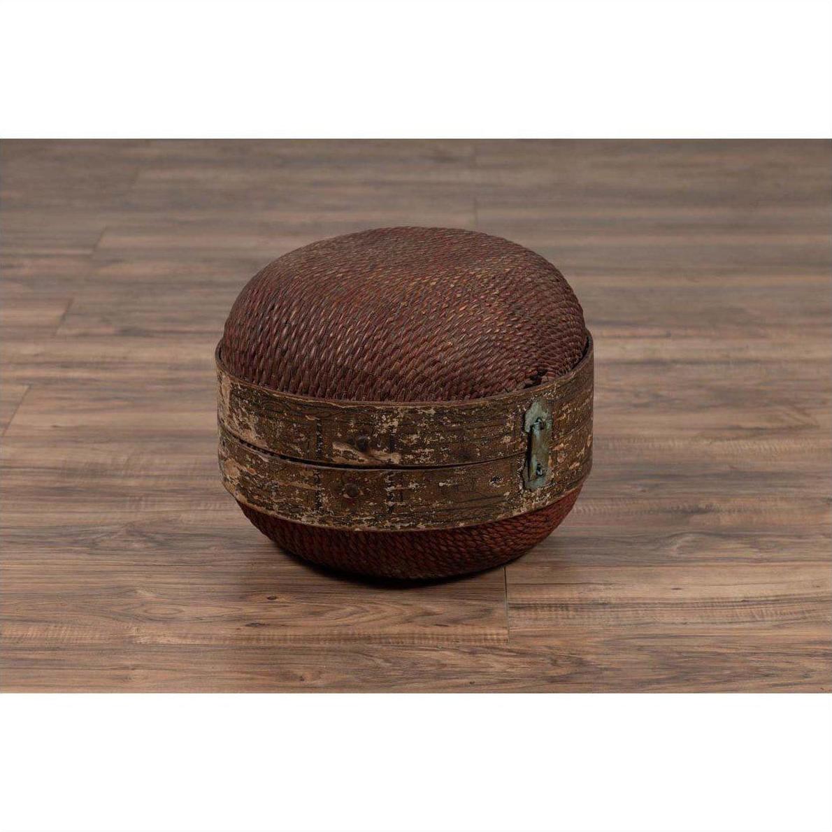 Brown rattan circular hat box with weathered patina on wood floor indoors.