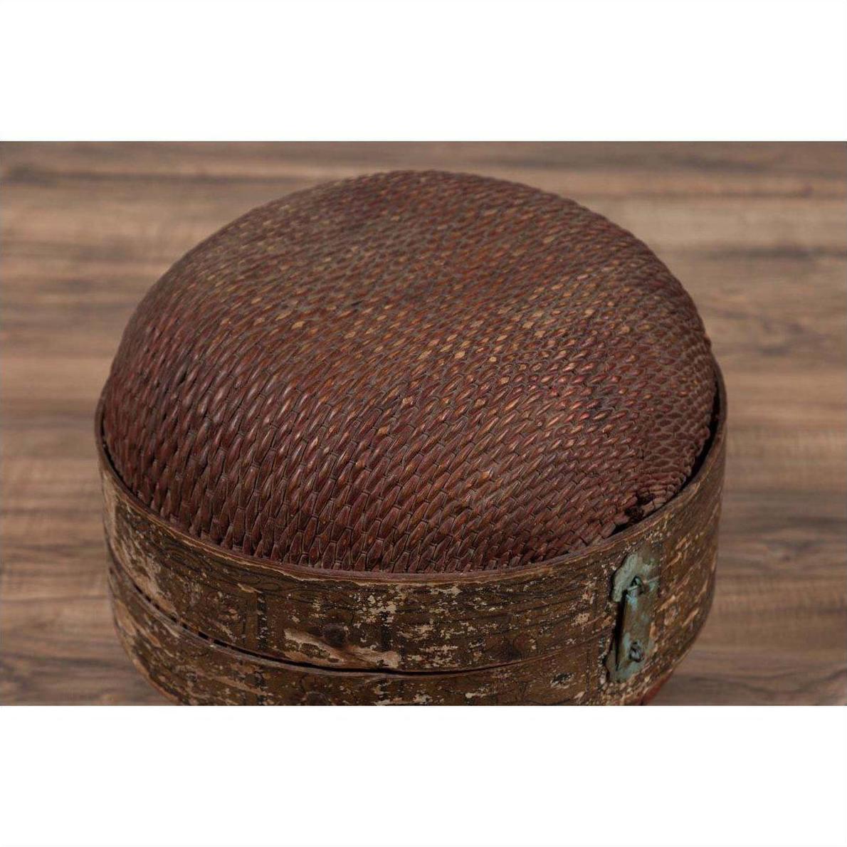 Brown rattan circular hat box with weathered patina on wooden surface.