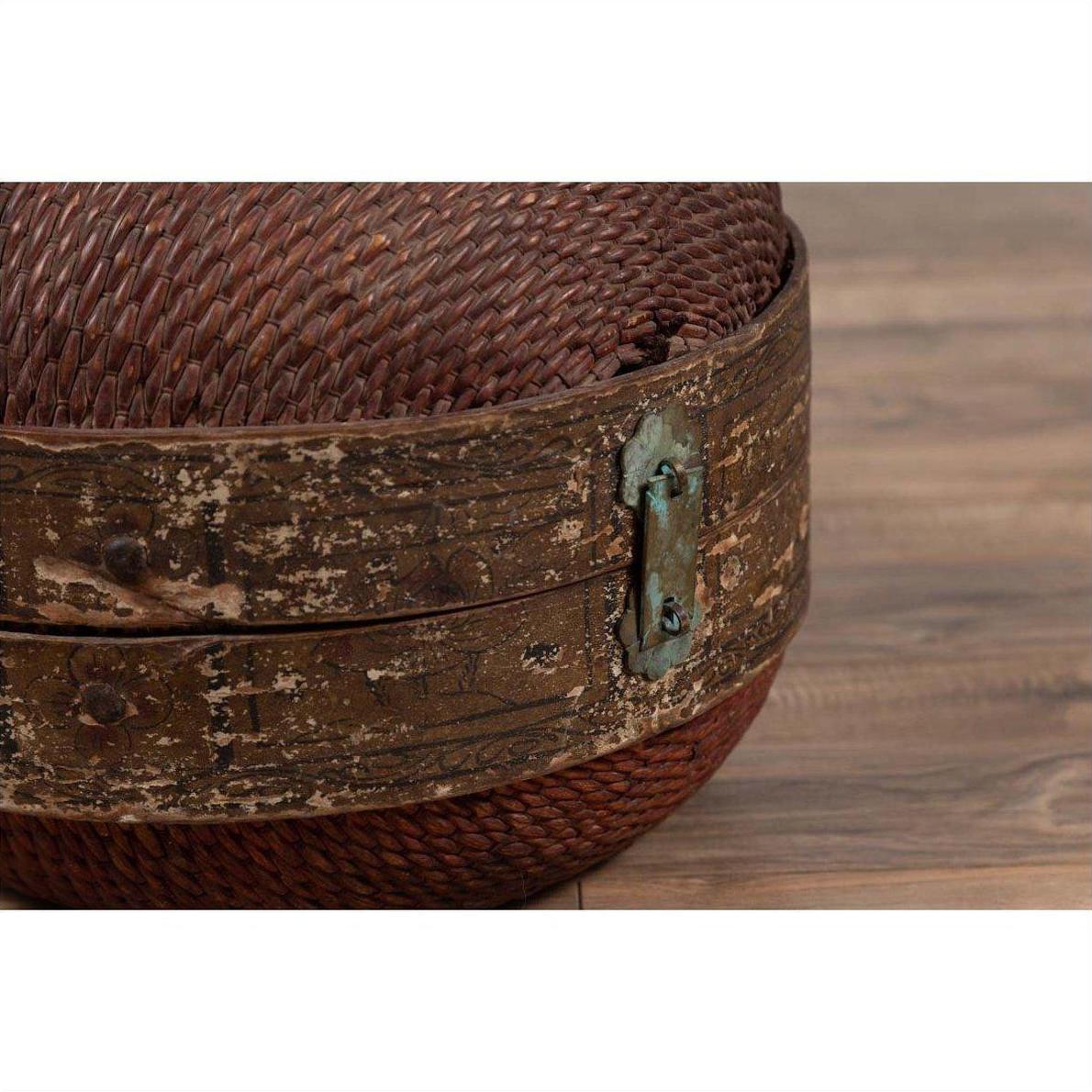 Close-up of a brown rattan circular hat box with weathered patina on a wooden floor.