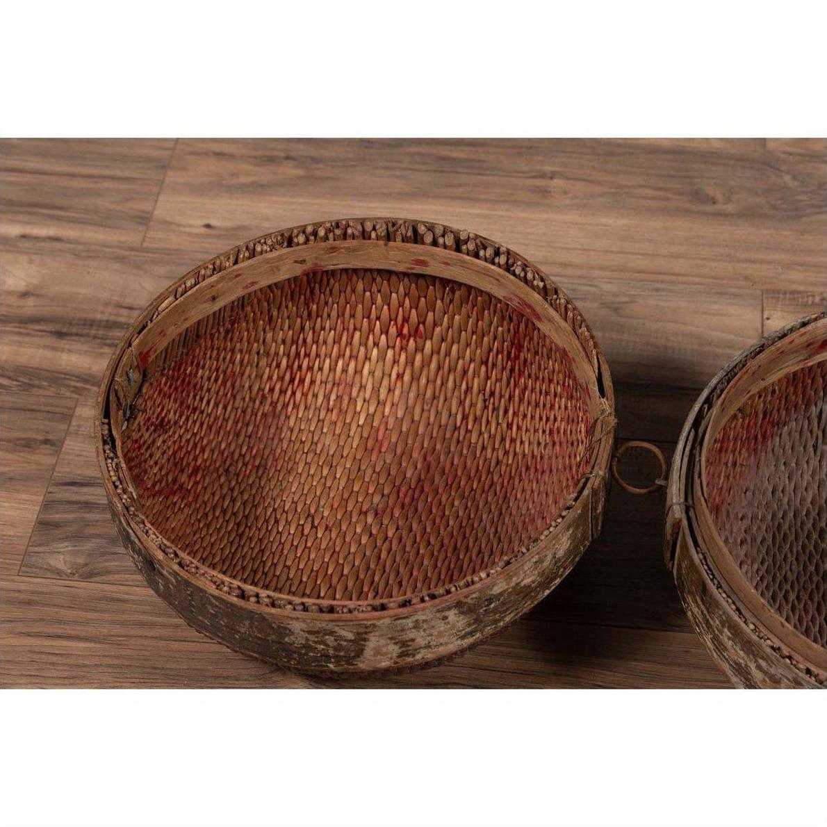 Brown rattan circular hat box with weathered patina on rustic wooden floor.