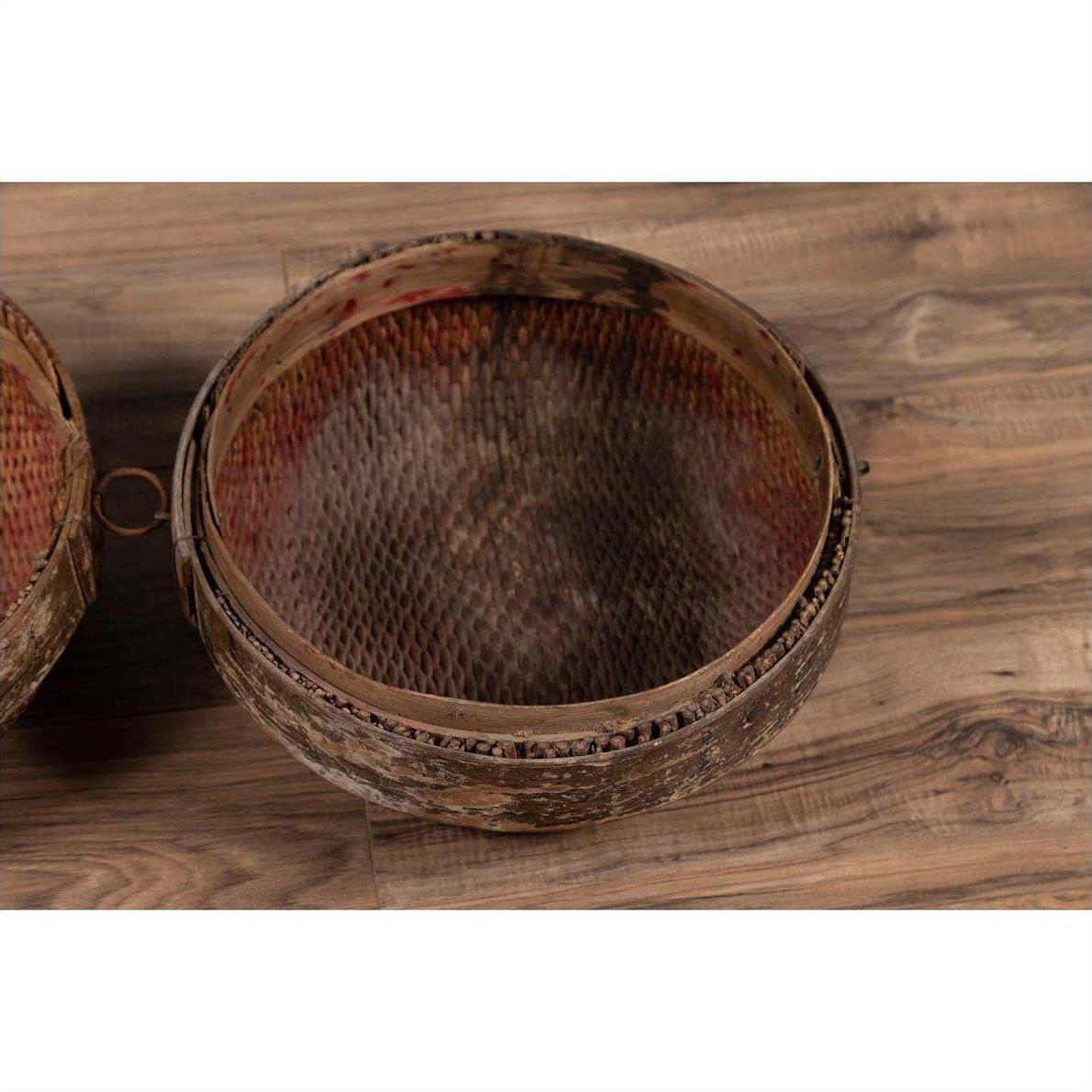 Brown rattan circular hat box with weathered patina on a wood-patterned floor indoors.