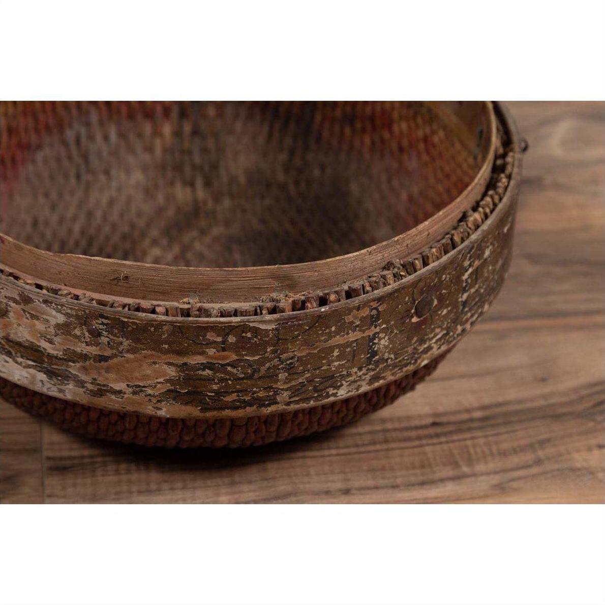 Brown rattan circular hat box close-up with weathered patina, shown on a wooden floor.