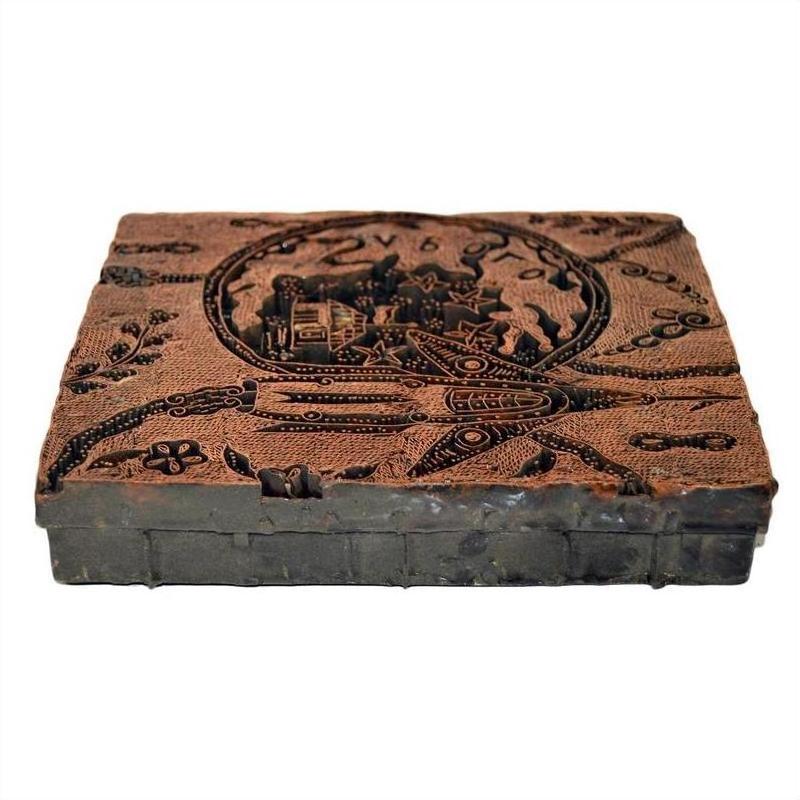 Close-up of vintage copper Batek ink block stamp with carved designs and Cyrillic text, used for printing or stamping.