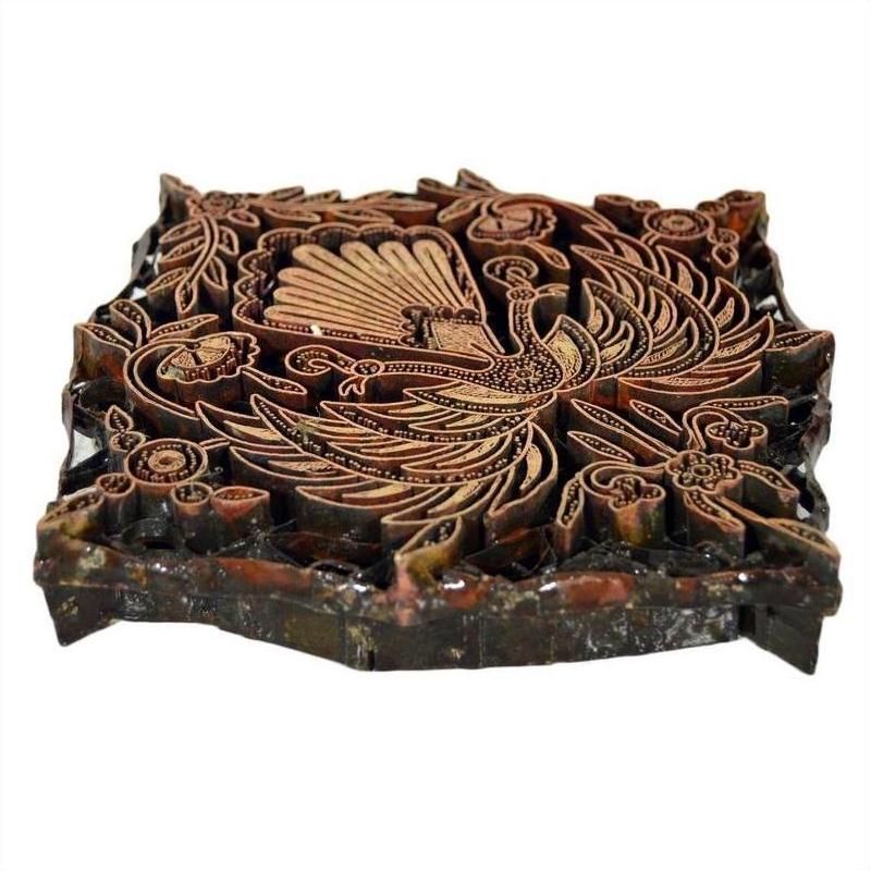 Vintage copper Batek ink block with peacock and floral motif, close-up of carved surface for textile or paper printing.