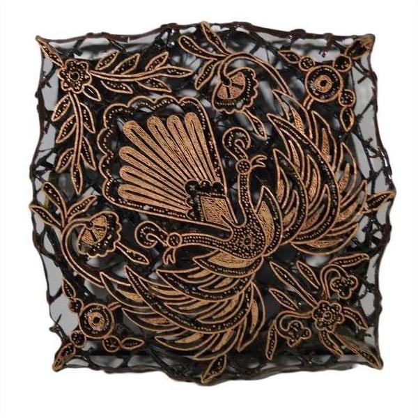 Close-up of vintage copper ink block with black and gold peacock and floral motifs, textured square design.