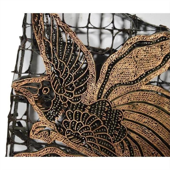 Close-up of a vintage copper Batek ink block featuring an intricately carved gold bird design on a dark mesh background.