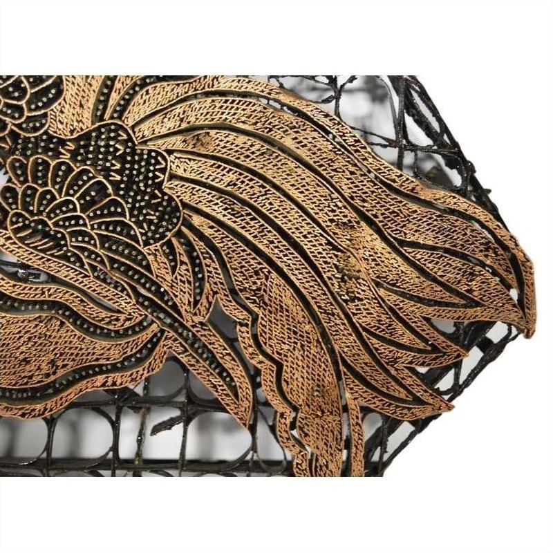 Close-up of vintage copper batik ink block with intricate golden-brown pattern on black lattice background.