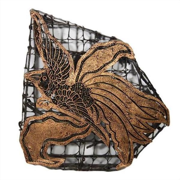 Close-up of a vintage copper Batek ink block with intricate patterns on a wire mesh background.