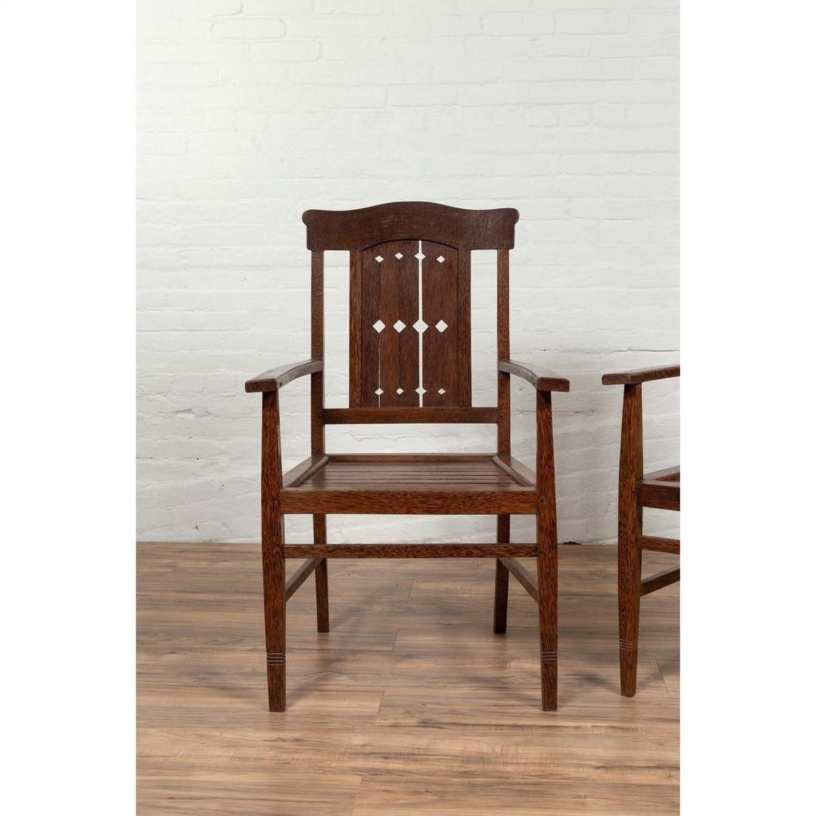 Brown wood Dutch Colonial armchair with pierced slats and bonnet rail on a wooden floor indoors.