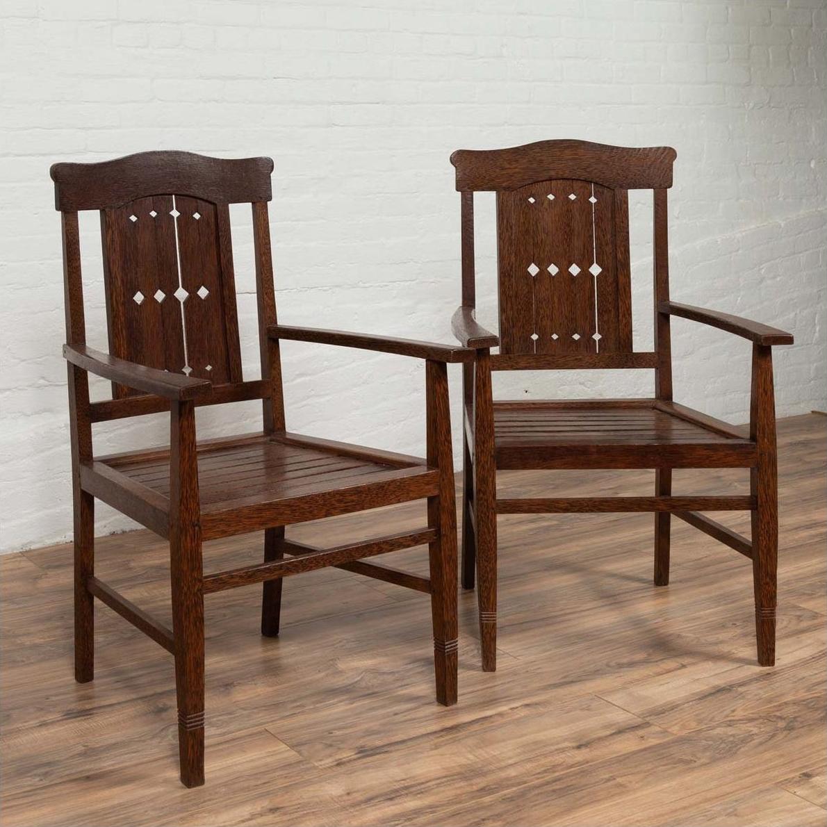Brown wood Dutch Colonial armchairs with pierced slats and bonnet rails on a wooden floor indoors.