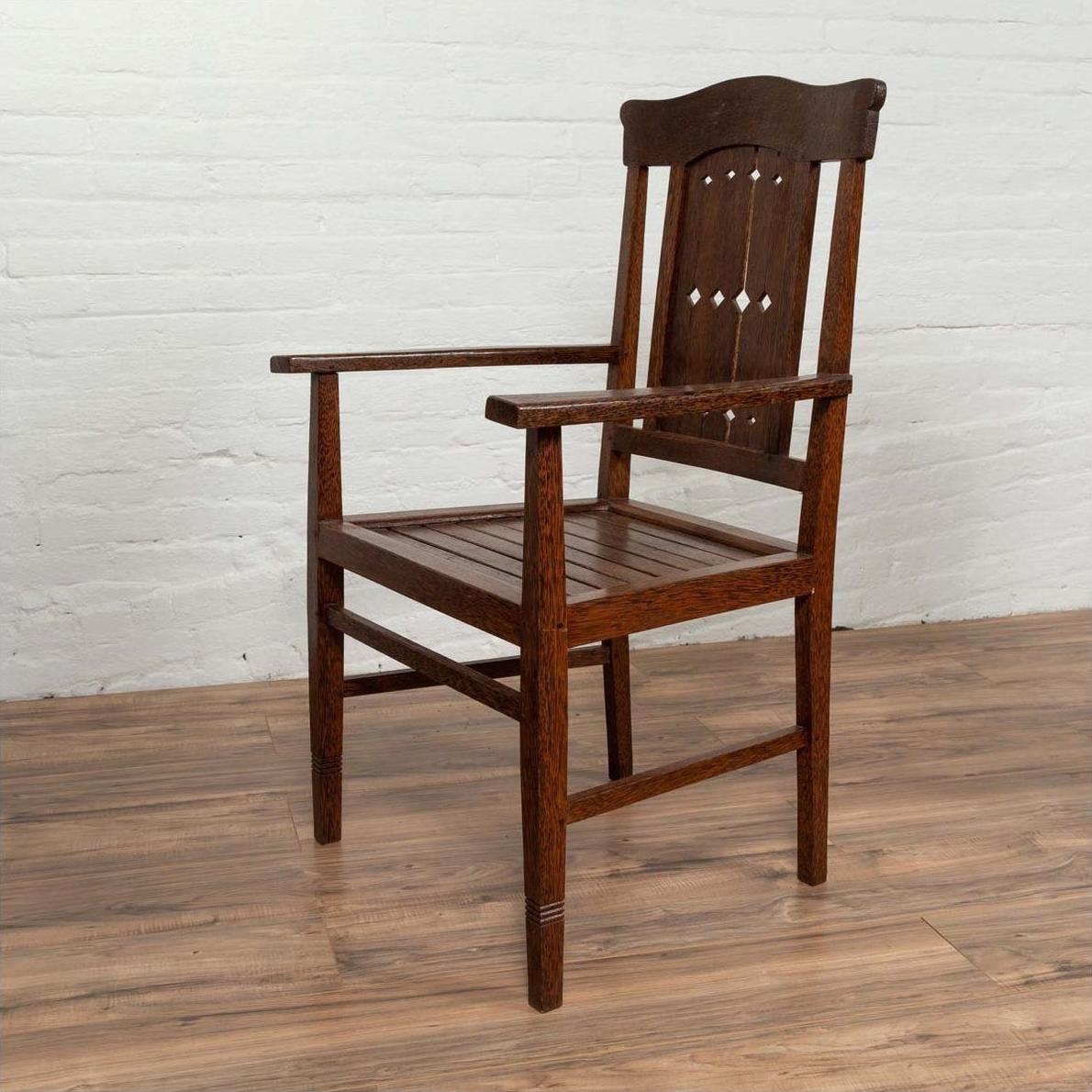 Brown wooden Dutch Colonial armchair with pierced slats and bonnet-style rail on wood floor indoors.