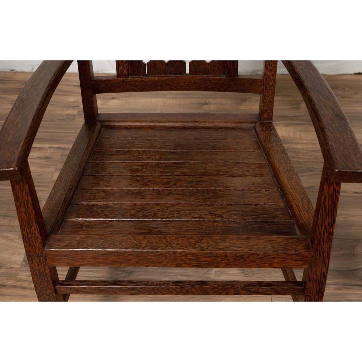 Brown wooden Dutch Colonial armchair with pierced slats and bonnet-style rail on wooden floor indoors.