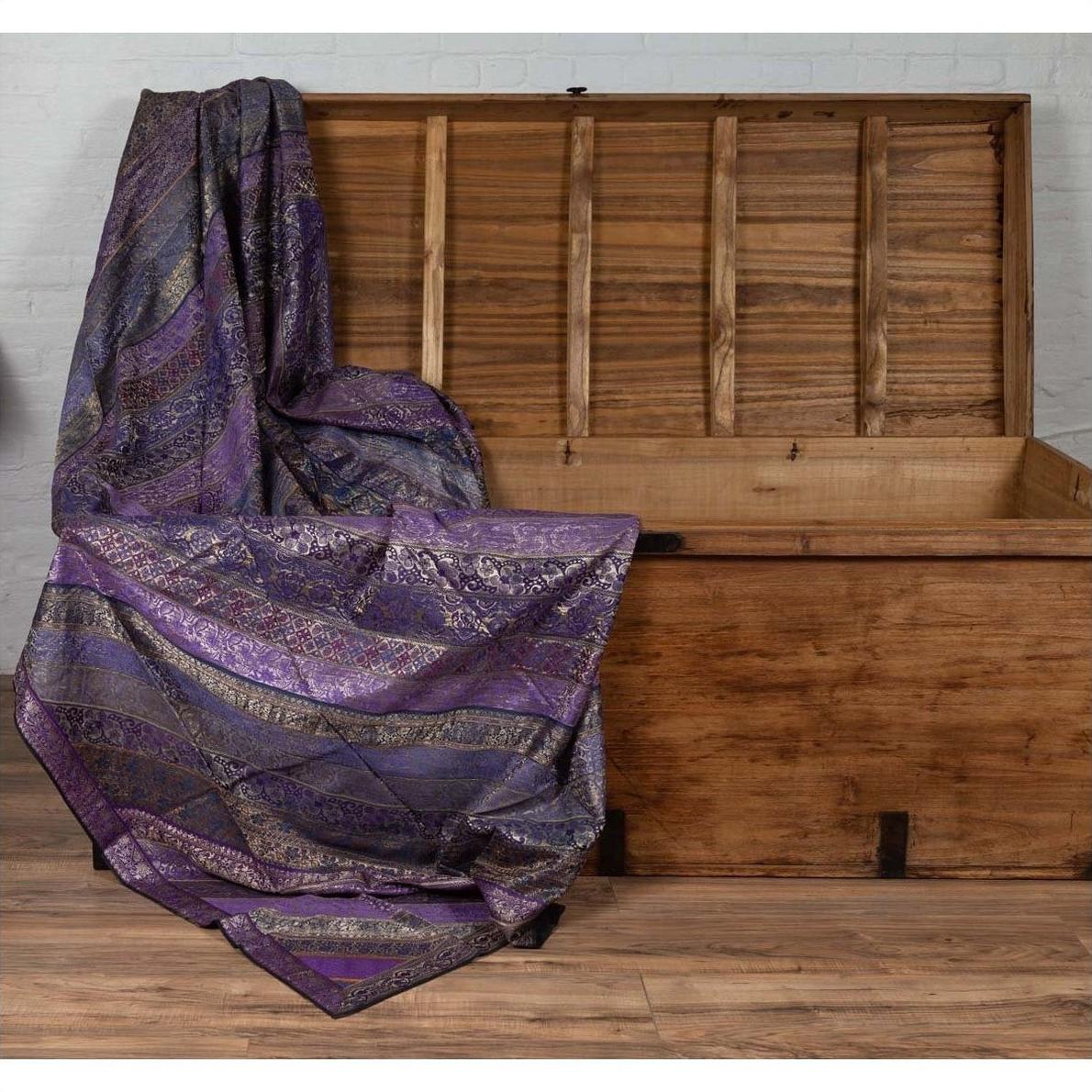 Purple silk embroidered fabric with silver and gold accents draped over an open wooden chest.