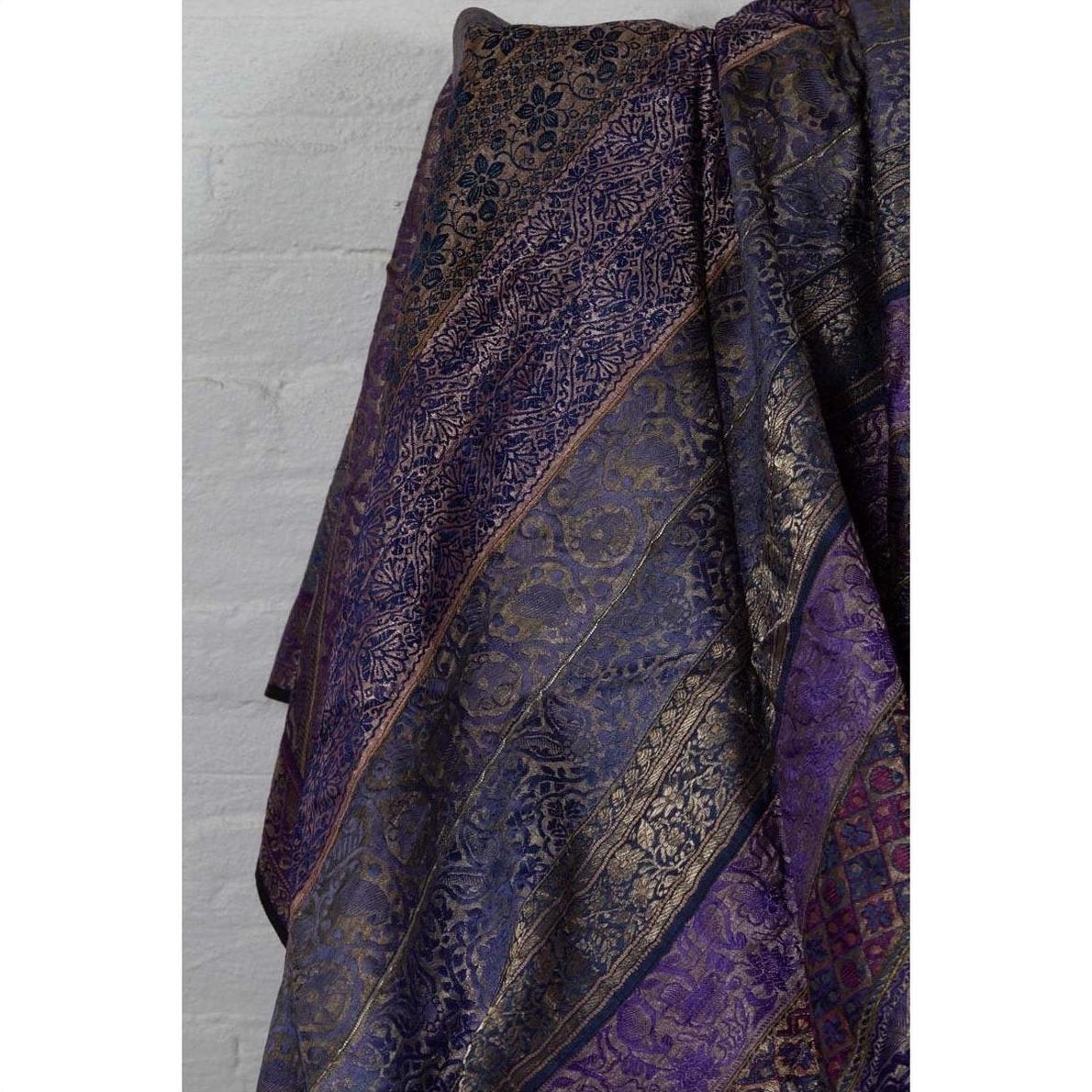 Purple silk fabric with purple, silver, and gold embroidery, displayed against a light-colored wall.