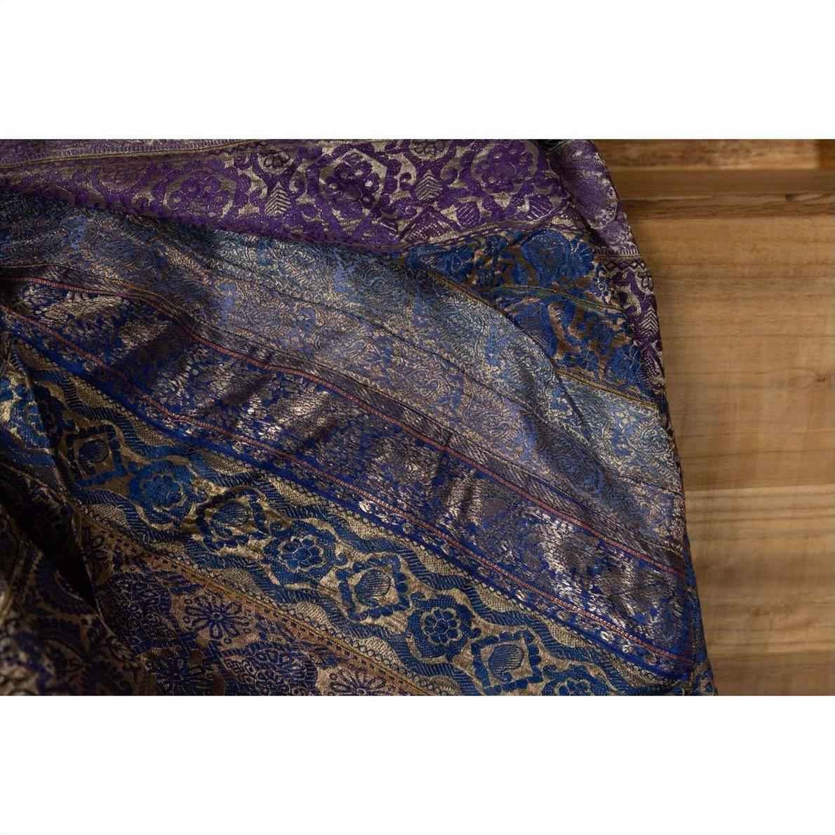 Close-up of purple silk fabric with purple, silver, and gold embroidery on a wooden surface.
