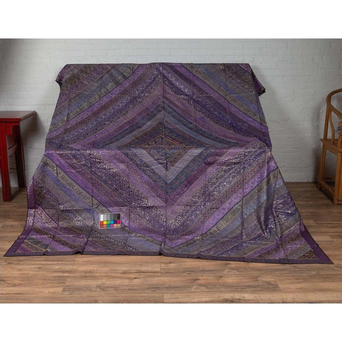 Purple silk embroidered fabric with silver and gold accents draped on a stand indoors.