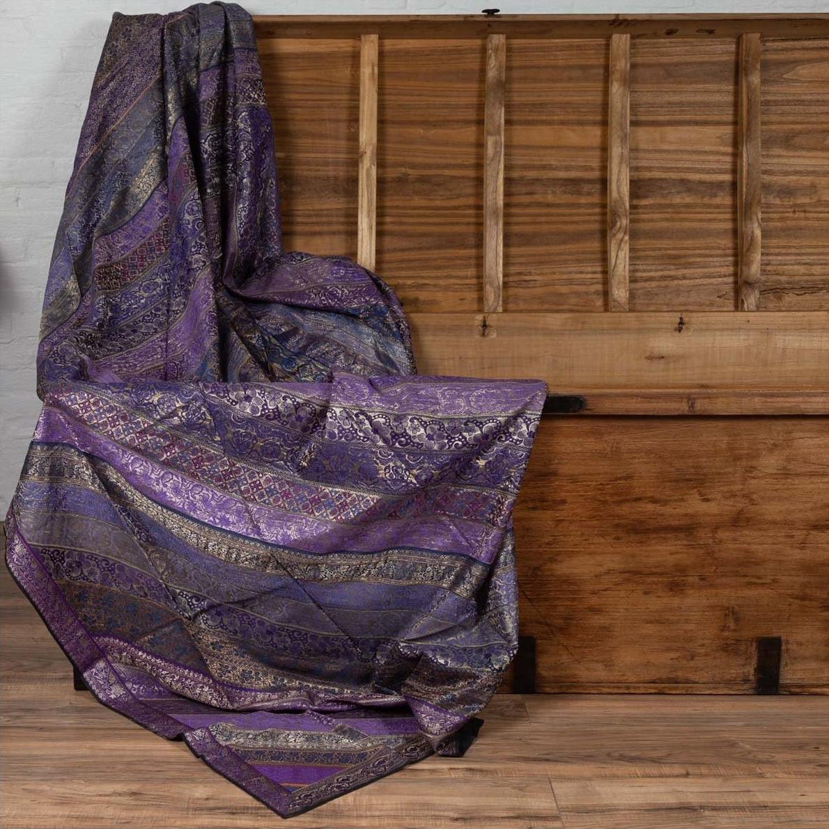 Purple silk fabric with silver and gold embroidery draped over a wooden chest on the floor.