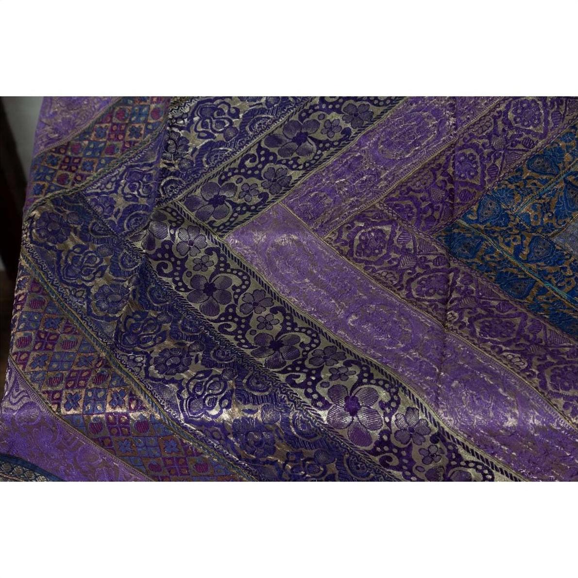 Close-up of purple silk fabric with silver and gold embroidery in detailed patterns.