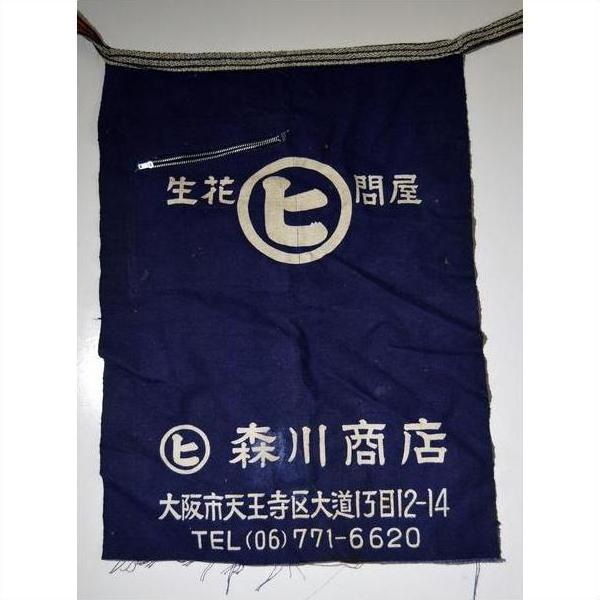Dark blue wax-printed cotton Japanese apron with white kanji, circular logo, and top zippered pocket, close-up view.