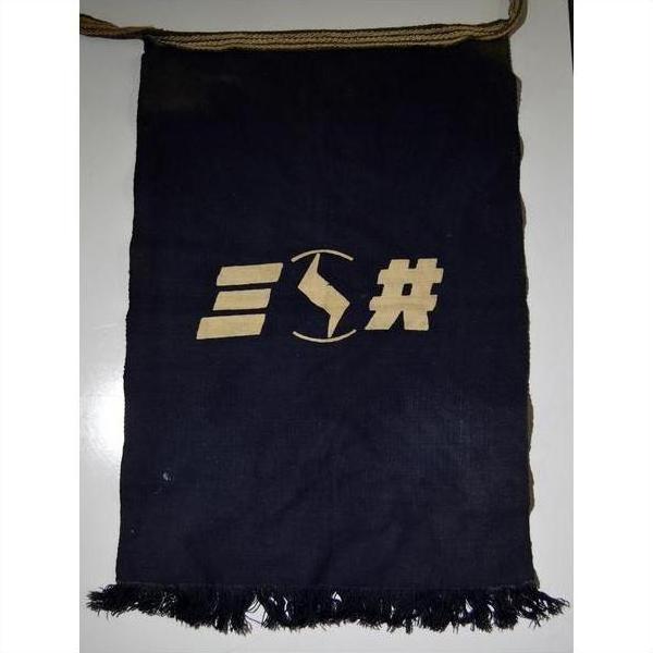 Black fabric apron with fringed edges and a tan geometric design at the center, close-up.