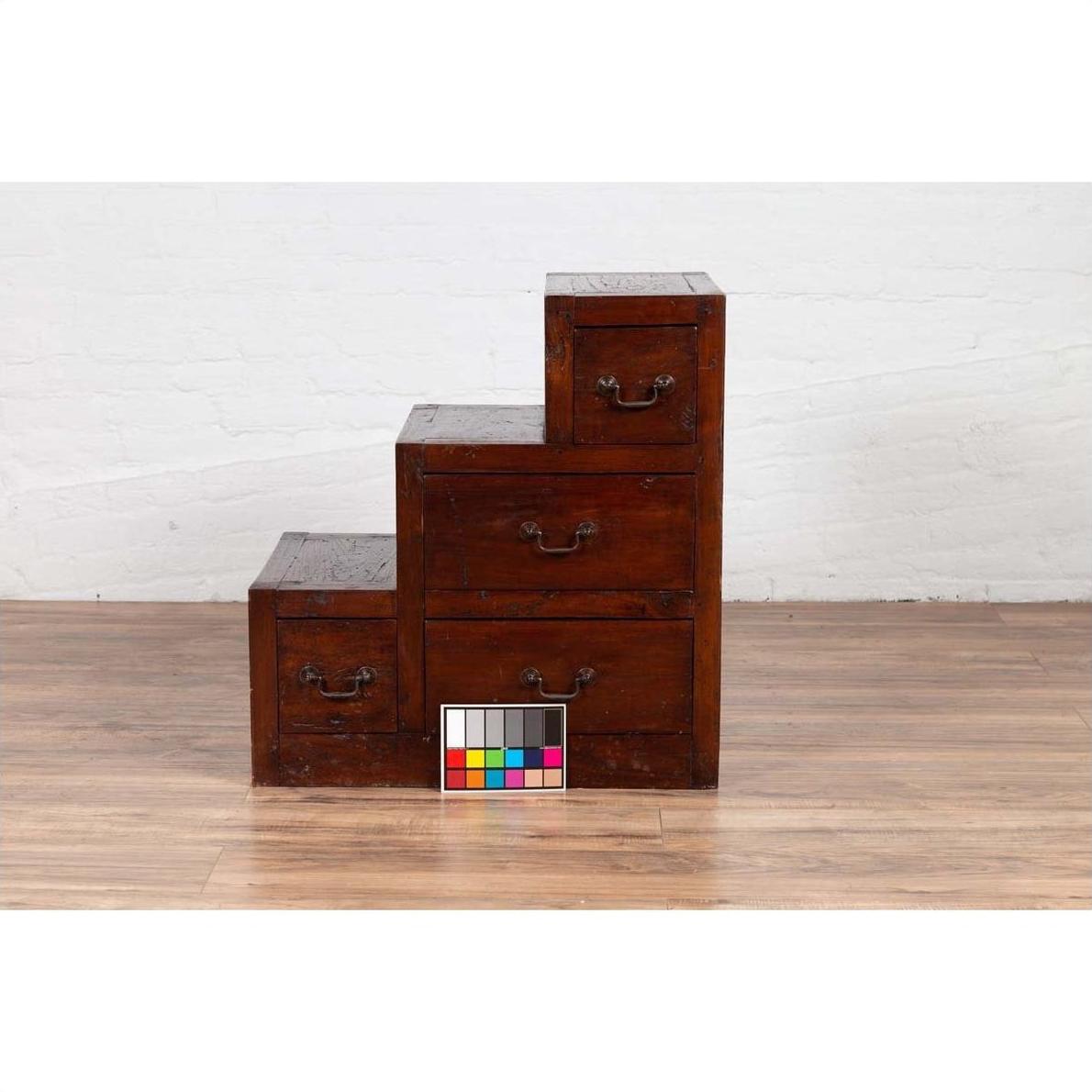 Brown wood staircase tansu cabinet with four drawers on wooden floor, color chart in front.