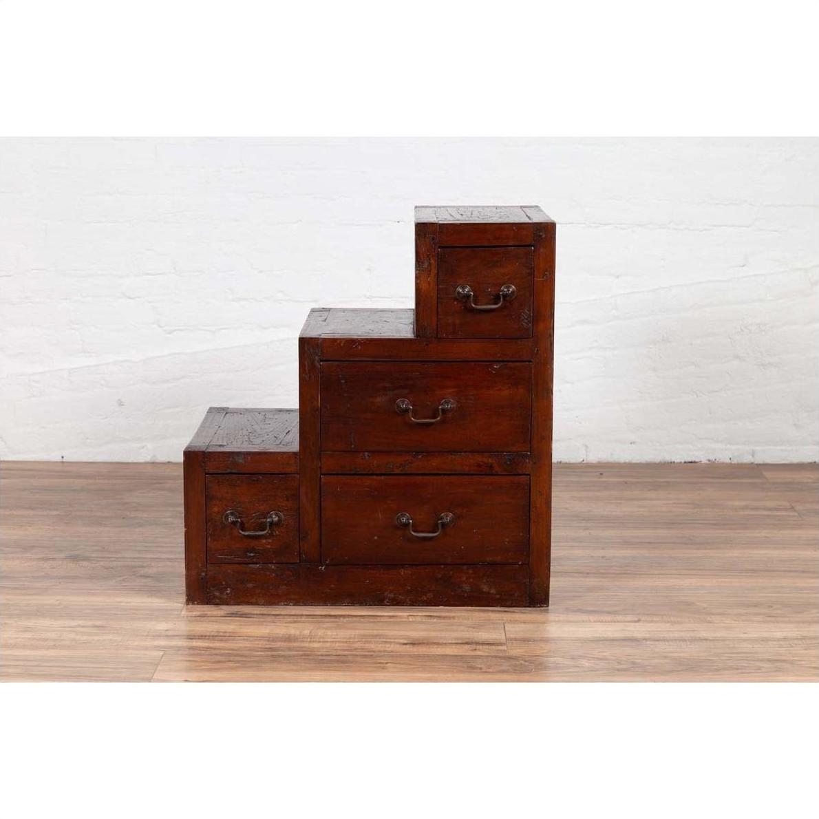 Brown wood staircase-style tansu cabinet with four drawers on wooden floor against white wall indoors.